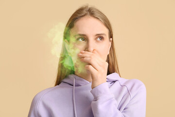 Young woman feeling disgusting smell on beige background