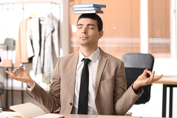 Young businessman with books meditating in office. Balance concept