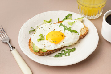 Delicious sandwich with fried egg, avocado and arugula on beige background