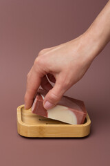 Obraz premium Female hand takes natural multicolored handmade solid soap from bamboo soap dish on mocha mousse background. Natural and eco-friendly handmade cosmetics. Natural spa products and bathroom decor