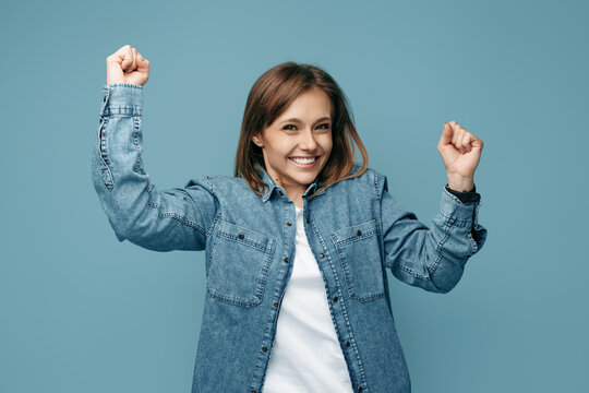 Cheerful young woman in jeans shirt celebrate success over blue background. Look in camera.