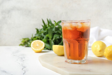 Board with glass of ice tea and lemons on white background