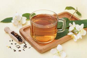 Cup of aromatic tea, dried leaves and beautiful jasmine flowers on color background