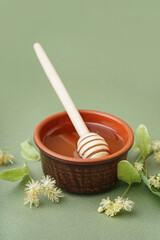Bowl with linden honey and dipper on green background