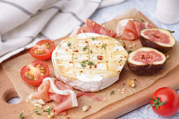 Wooden board with tasty baked Camembert cheese on table