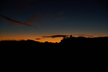 A stunning silhouette of grassy hills and a fence at sunset, with a vibrant gradient of orange and deep blue in the sky, creating a peaceful and dramatic twilight scene.