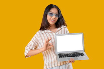 Naklejka premium Young female Asian programmer with laptop showing OK gesture on yellow background