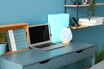 Fototapeta premium Stylish workplace with modern laptop, stationery and lamp near color wall