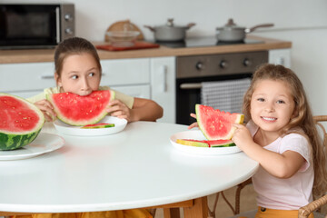 Happy little girls with slices of fresh watermelon sitting at table in kitchen