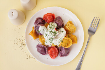 Plate of boiled colorful dumplings with sour cream and dill on yellow background