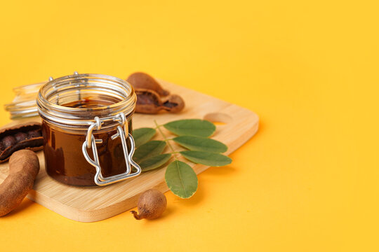 Jar with tasty tamarind jam with fruits on orange background