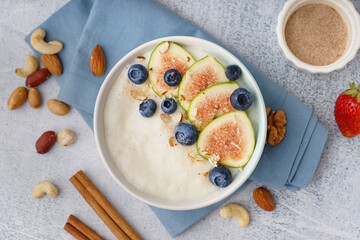 Bowl of tasty semolina porridge with berries and figs on white background
