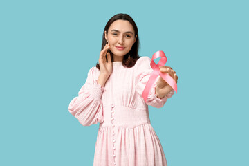 Pretty young woman holding pink ribbon on blue background. Breast cancer awareness concept