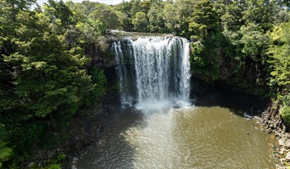 Stunning aerial view of a powerful waterfall cascading down a rocky cliff face, surrounded by lush green forest. Nature's beauty. Rainbow Falls, Kerikeri, Northland, NZ