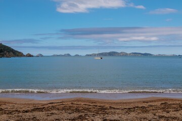 Tranquil coastal scene. Gentle waves lap a pebble beach, with a sailboat anchored in the bay. Peaceful day. Mahinepua Bay, Kaeo, Northland, NZ
