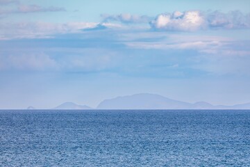 Calm ocean waters meet a hazy mountain range on the horizon. Peaceful, tranquil scene. Matauri Bay, Matauri Bay, Northland, NZ