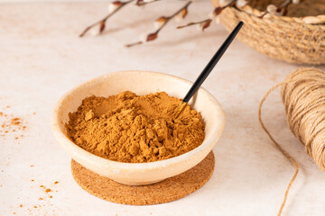 A small bowl filled with cinnamon powder sits on a cork coaster, with willow branches in the background.