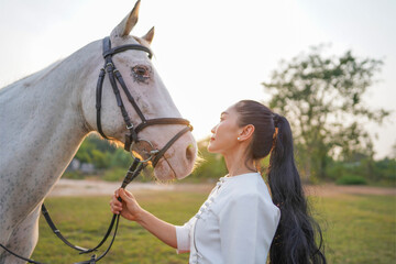 Obraz premium Asian woman wearing Chinese dress holding a bow and a white horse at the end of the sunset