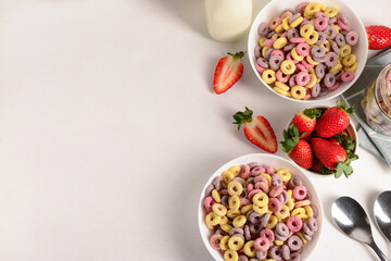 Bowls with colorful sweet cereal rings and strawberries on white table