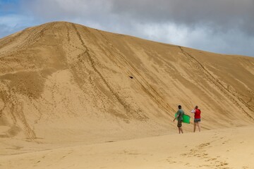 Couple sandboarding down a large dune. Fun in the sun. Te Paki Giant Sand Dunes, Cape Reinga, Northland, NZ