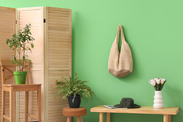Interior of beautiful hall with bench, houseplant and bouquet of flowers near green wall