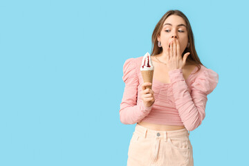 Surprised young woman holding ice cream in waffle cone on blue background