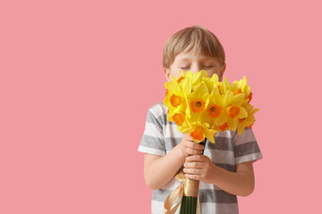 Cute little happy boy with bouquet of beautiful narcissus on pink background