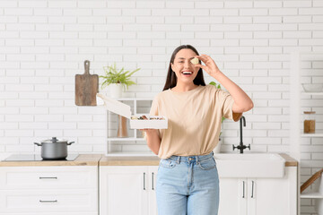 Happy young woman holding box with chocolate covered strawberries in kitchen