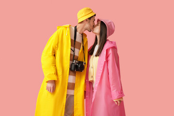 Young couple in raincoats kissing on pink background