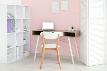 Interior of stylish office with workplace, laptop, chair and shelving unit