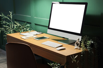 Stylish workplace with modern computer near green wall in office at night