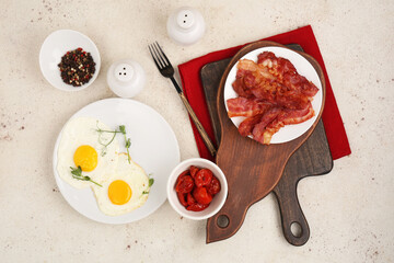 Plates with fried eggs and bacon on board on white background. Top view