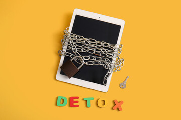 Modern tablet computer with chain, padlock, key and word DETOX on yellow background