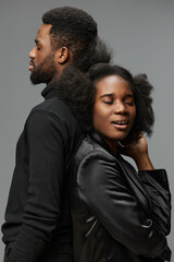 Obraz premium A stylish couple with natural textured hair pose back to back, showcasing confidence and intimacy in a modern studio setting with a neutral background