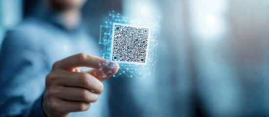 Close-up of hand holding digital QR code with futuristic glowing interface in a blurred background