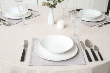 Minimalist table setting with white tablecloth, plates, glasses, cutlery and vase in dining room