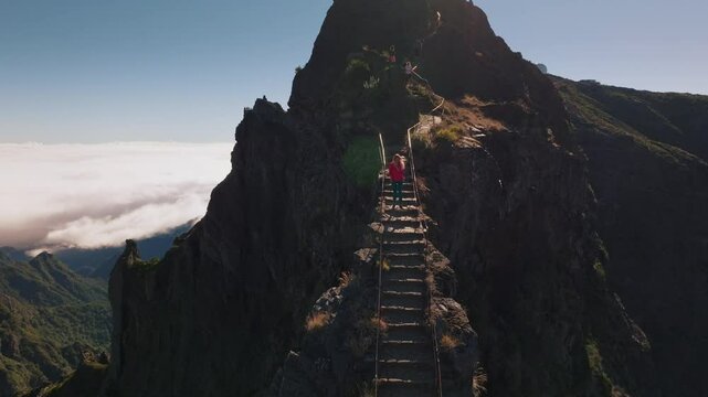 Aerial view of blonde woman hiking trail path and climbing Pico Ruivo mountain in Madeira. Young adult adventure journey in nature. Travel exploring Madeira Island, Portugal