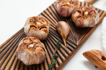 Wooden board with baked garlic and thyme on white background