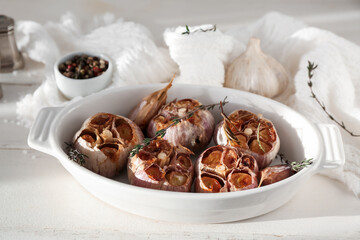 Baking dish with garlic, rosemary and thyme on white wooden background