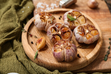 Board with baked garlic, thyme, rosemary and peppercorns, closeup