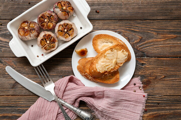 Baking dish with garlic, peppercorns and croutons on wooden background