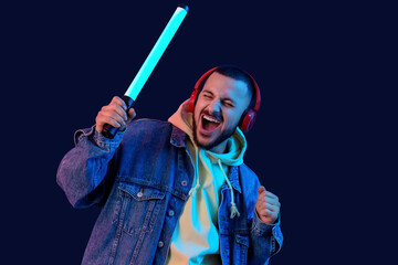 Young man in headphones with neon lamp singing on dark blue background