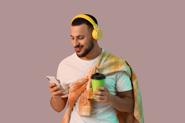 Young man in headphones with coffee cup using mobile phone on grey background