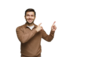 Smiling man in a brown sweater pointing upward while standing against a plain backdrop