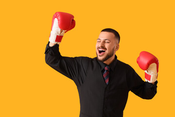 Happy businessman with boxing gloves on yellow background. Knockout concept