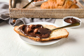Plate of sweet croissant with chocolate spread and hazelnuts on white background