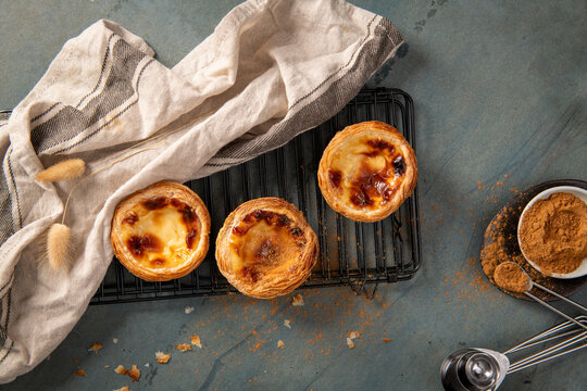Three freshly baked Portuguese custard tarts on a cooling rack