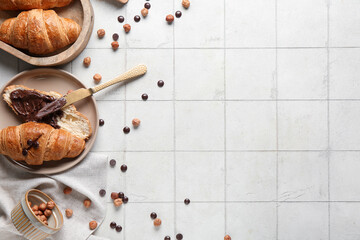 Plate of sweet croissants with chocolate spread and hazelnuts on white tile background