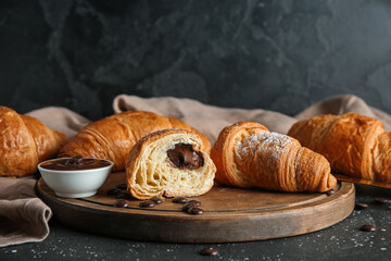 Wooden board with sweet chocolate croissants on black background