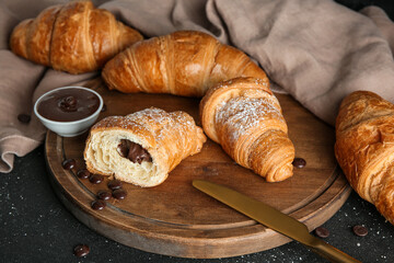 Wooden board with sweet chocolate croissants on black background